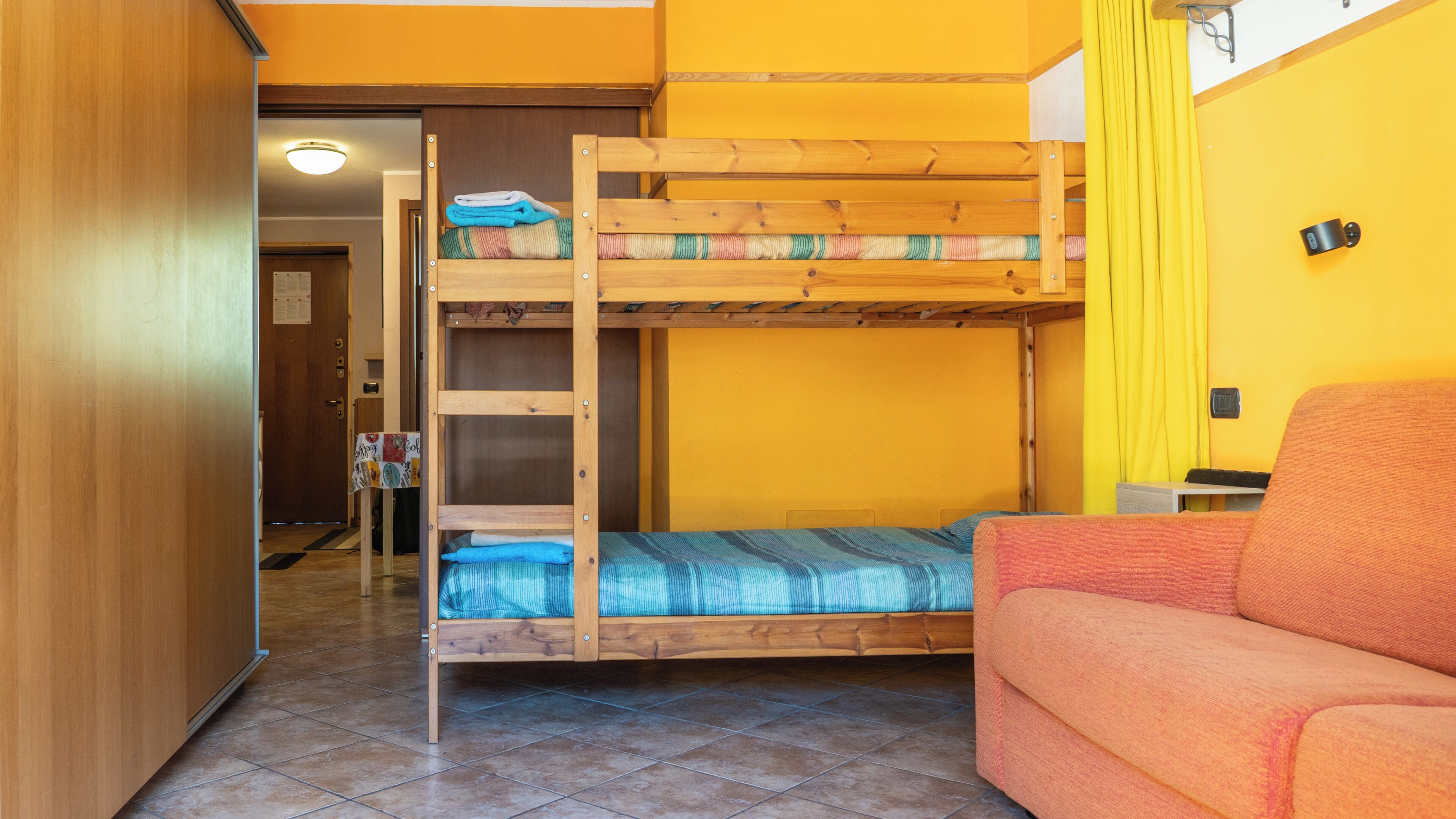Un lit superposé avec un lit en bas, un canapé et un mur jaune.