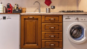 Una cocina con armarios de madera, lavadora, pileta y estufa.