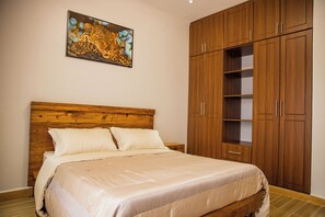 Ein Schlafzimmer mit einem Holzkopfteil, einem großen Bett mit weißer Bettwäsche, einem Holzschrank mit mehreren Regalen und einem Leopardenbild an der Wand.