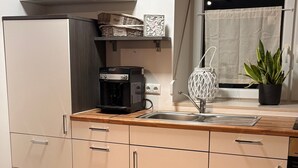 A kitchen with a built-in oven, a coffee machine, a sink, and a window with a curtain. - Cozy 60 m² Apartment with Terrace (Künzing)