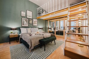 Une chambre à coucher comprenant un lit, des tables de chevet, un banc, une échelle et une vue sur une autre pièce, visible à travers une porte vitrée.