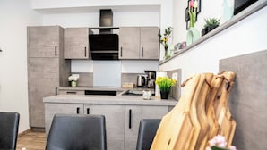 Una cocina moderna con armarios grises, una campana extractora negra y un comedor con mesa y sillas de madera.