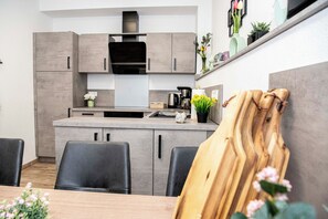 A modern kitchen with grey cabinets, a black range hood, and a dining area with a wooden table and chairs. - Seidenglanz ap. in the pedestrian zone of the historic old town of Dillenburg (Dillenburg)