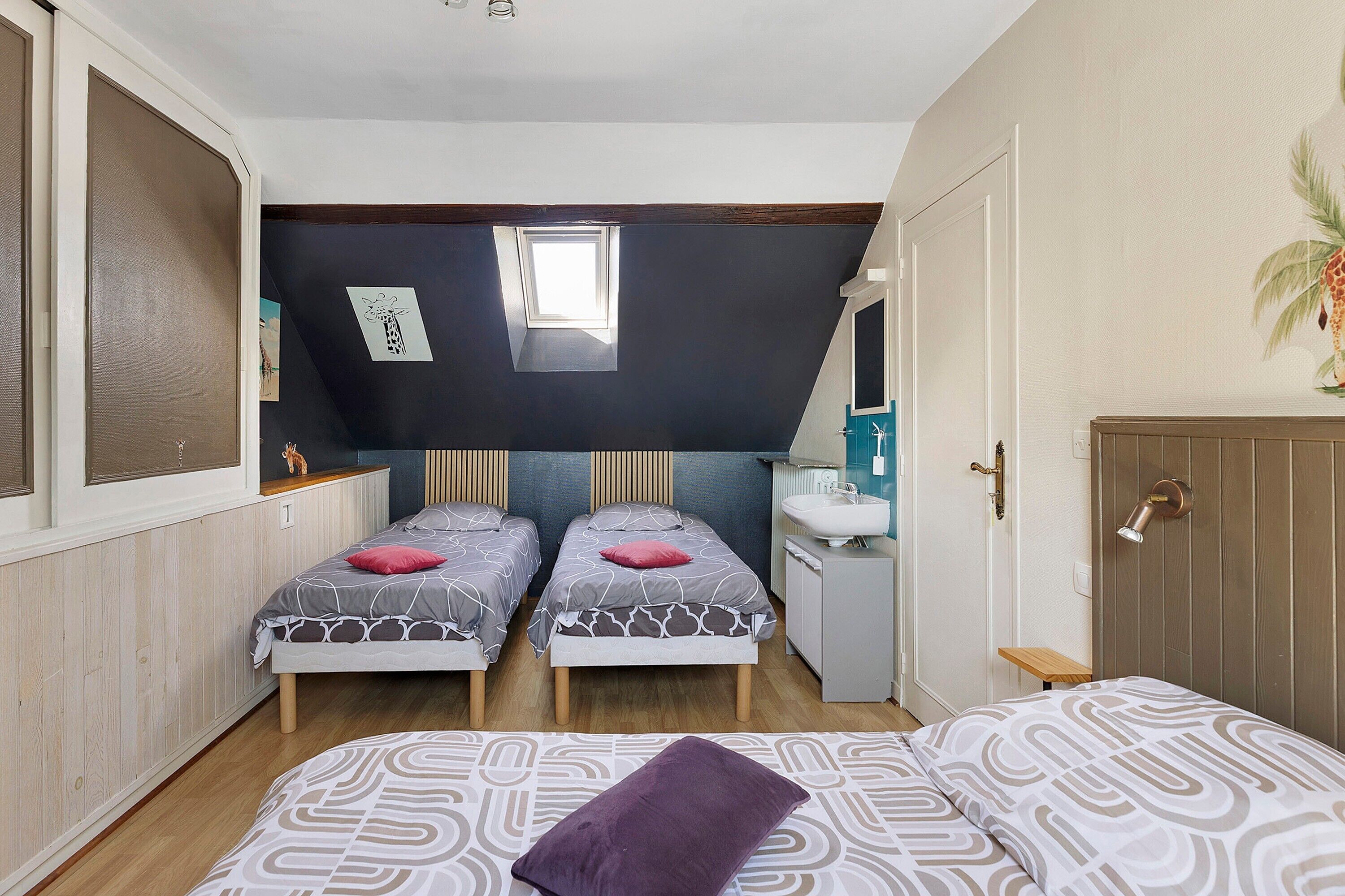 A bedroom with two beds, a window, a sink, and a door.