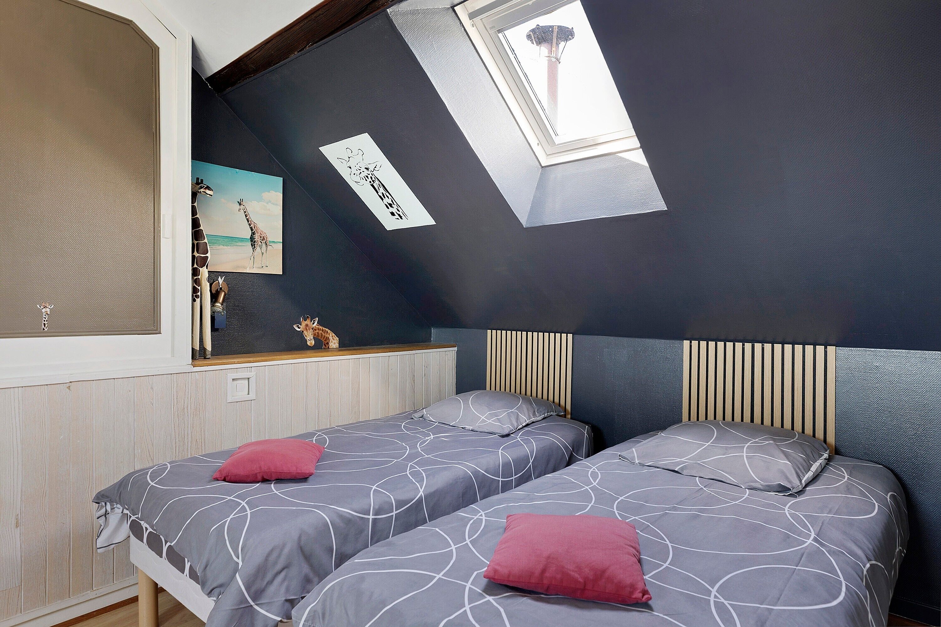 A bedroom with two beds, a skylight, a giraffe picture, and a view of a tower.