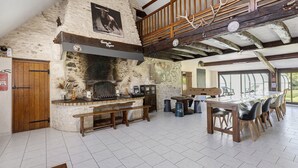 Un interior rústico con chimenea de piedra, vigas de madera, techo alto y un comedor con sillas y una mesa.