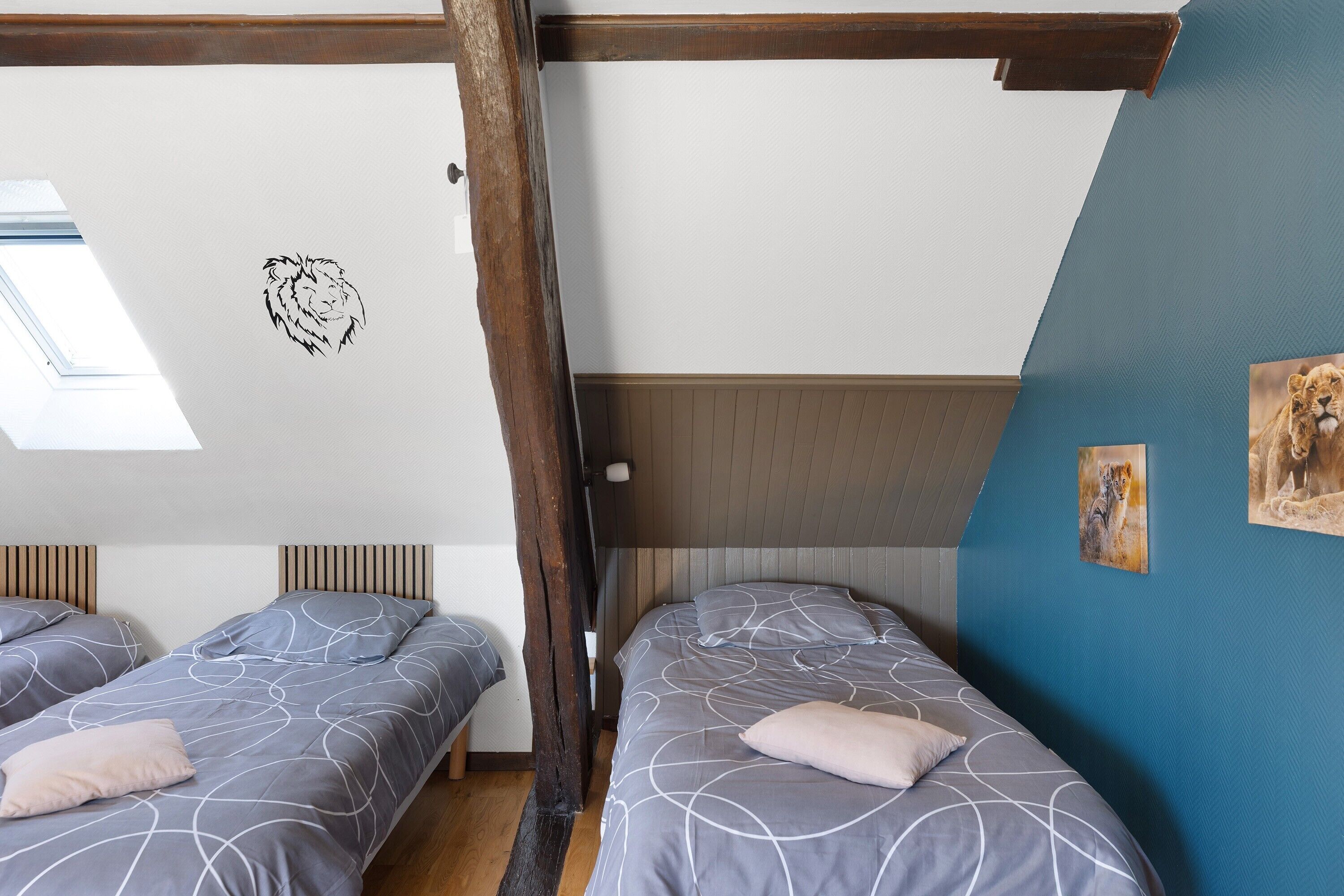 A bedroom with two beds, a sloped ceiling, wooden beams, a skylight, and wall art.