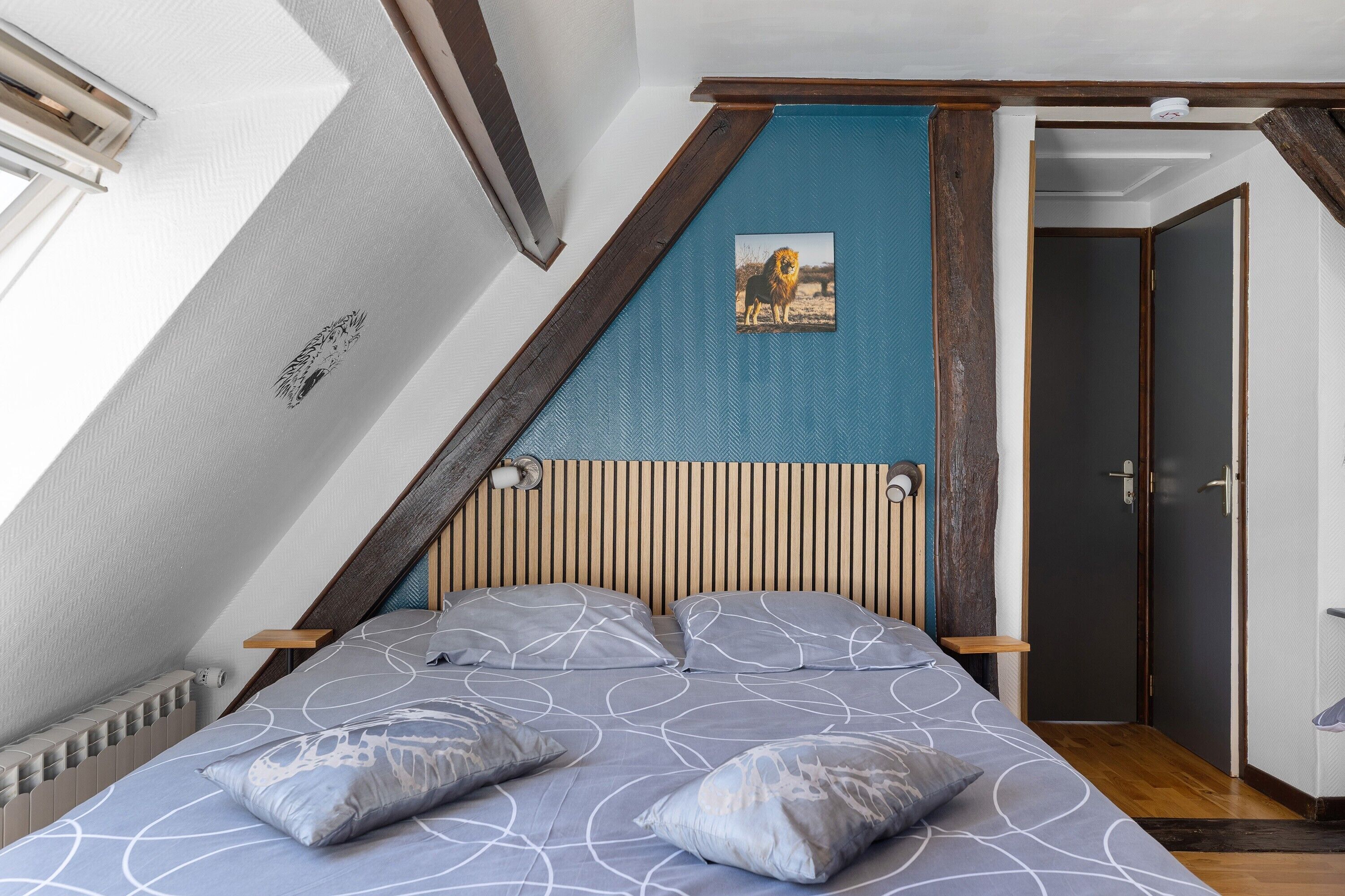 Un dormitorio con techo inclinado, una cama con ropa de cama estampada, cabecero de madera, un cuadro enmarcado en la pared y una puerta a la derecha.