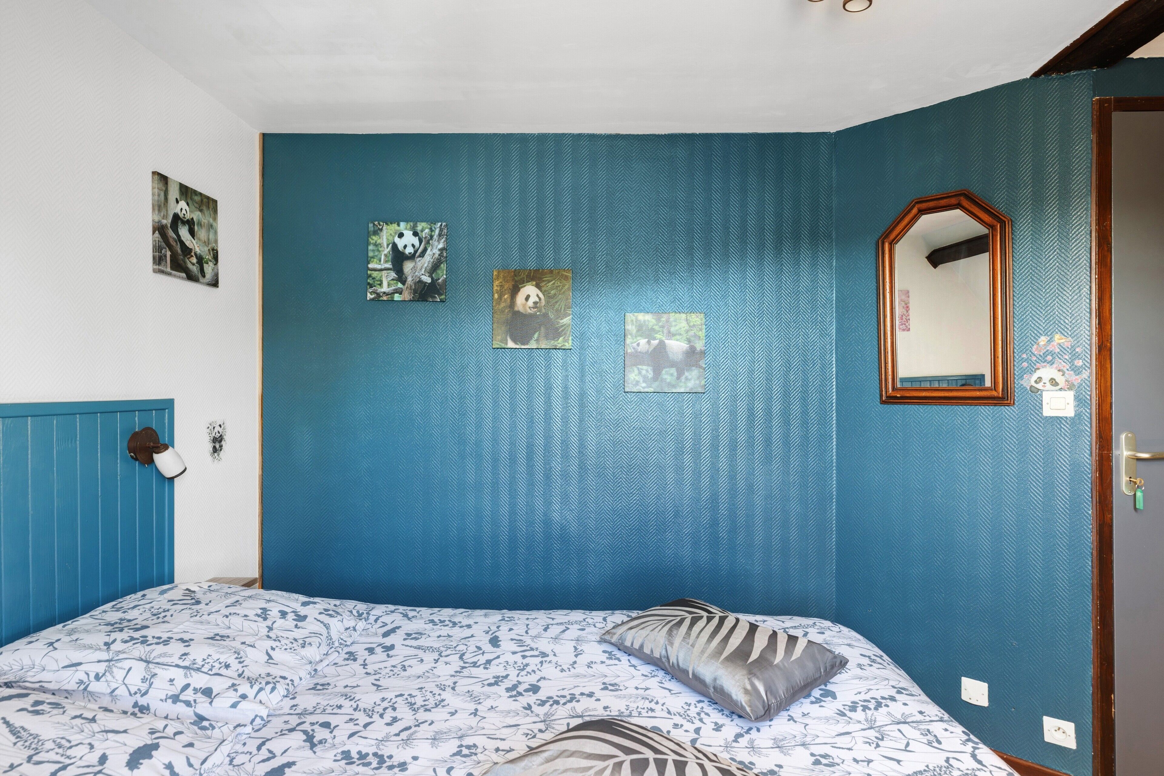 Un dormitorio con una cama, un espejo y tres cuadros con temática de panda en la pared.