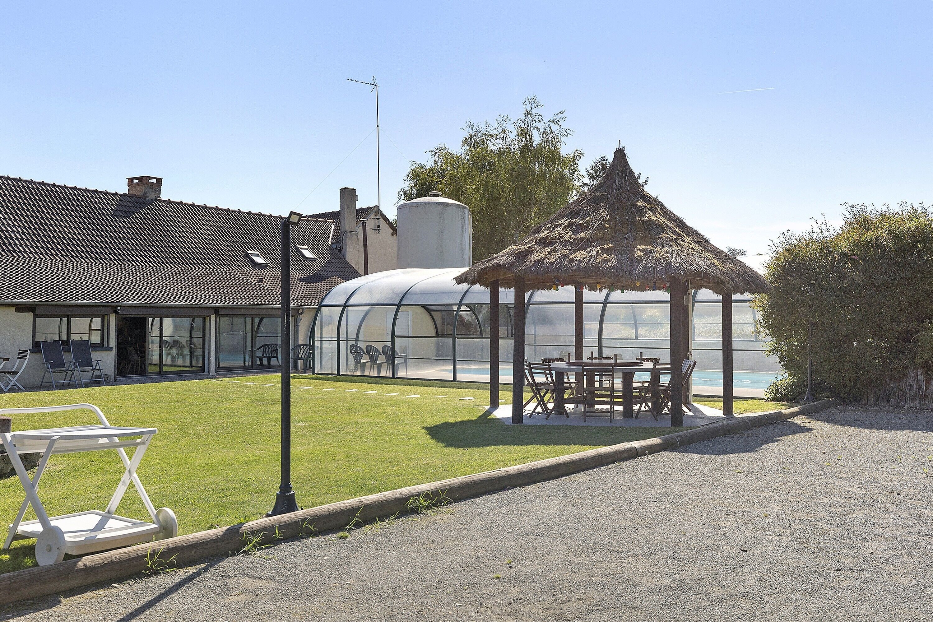 A greenhouse, a gazebo, and outdoor seating with a view of a building with a tiled roof.