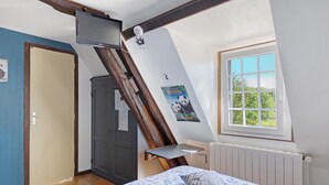 Une chambre avec un plafond en pente, un lit avec une literie à motifs, une fenêtre donnant sur un paysage agréable, une porte et une petite étagère.