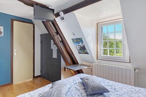 A bedroom with a sloped ceiling, a bed with patterned bedding, a window with a view, a door, and a small shelf.