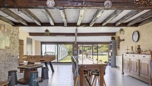 Une cuisine rustique avec des poutres apparentes, une grande table à manger et une vue sur l’extérieur.