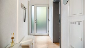 A hallway with a bench, a door with frosted glass, a mirror, and a wall-mounted light fixture.