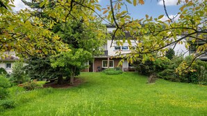 A residential property with a well-maintained lawn, a large tree, and a two-story building with a visible balcony.