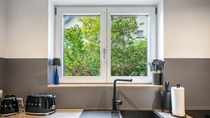 A modern kitchen with a window, two electric kettles, a sink, and a window shelf with kitchen utensils.