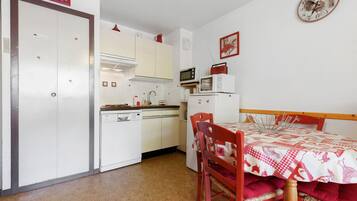 Een compacte keuken met witte kastjes, een magnetron, en een eethoek met een rode tafel en stoelen.