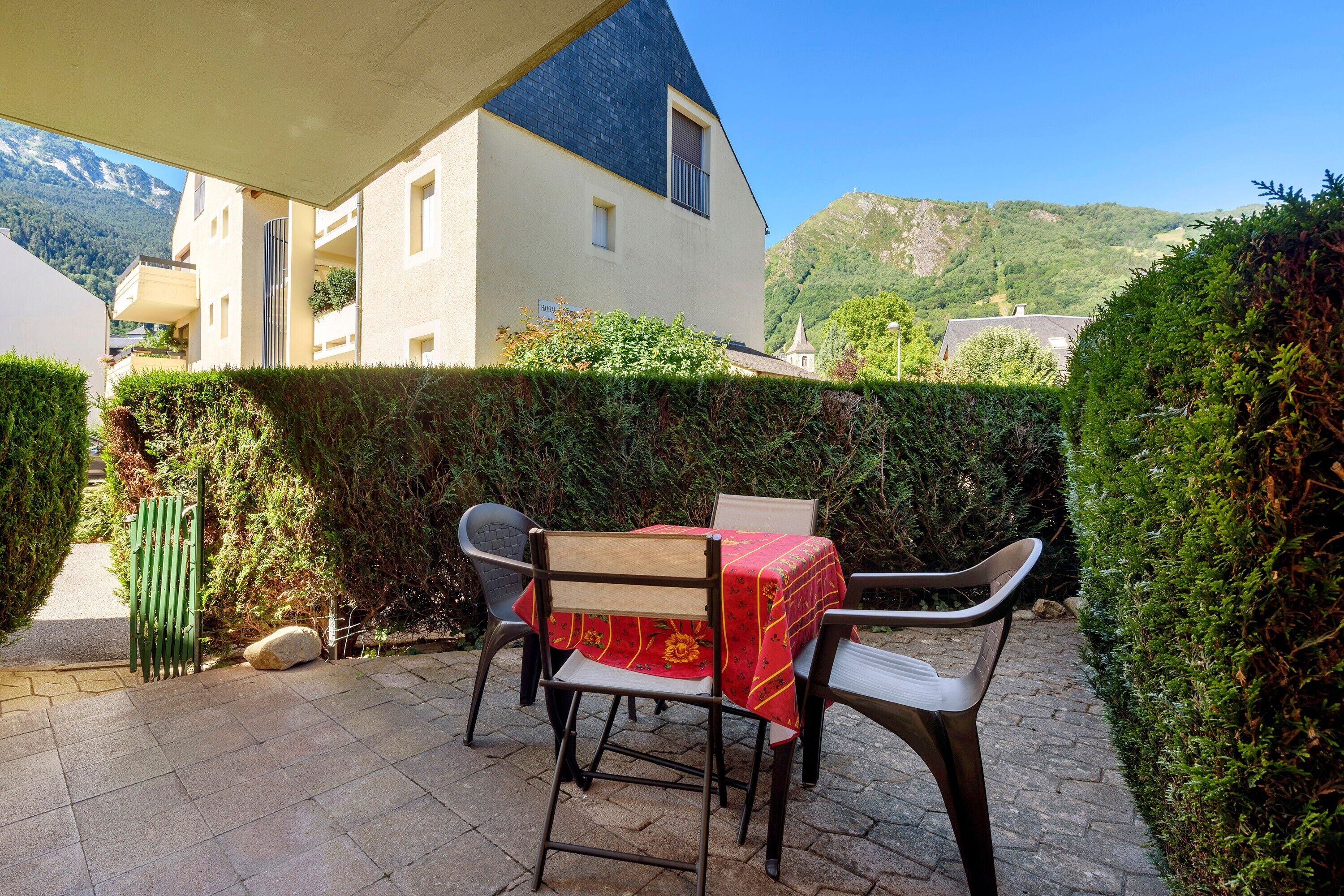 A patio with outdoor furniture and a table, a building with a balcony, and a mountain view in the background.