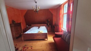 Ein Schlafzimmer mit einem hölzernen Bett, einem Holzschrank, einem Nachttisch, einem roten Sofa und einem Fenster mit Vorhängen.