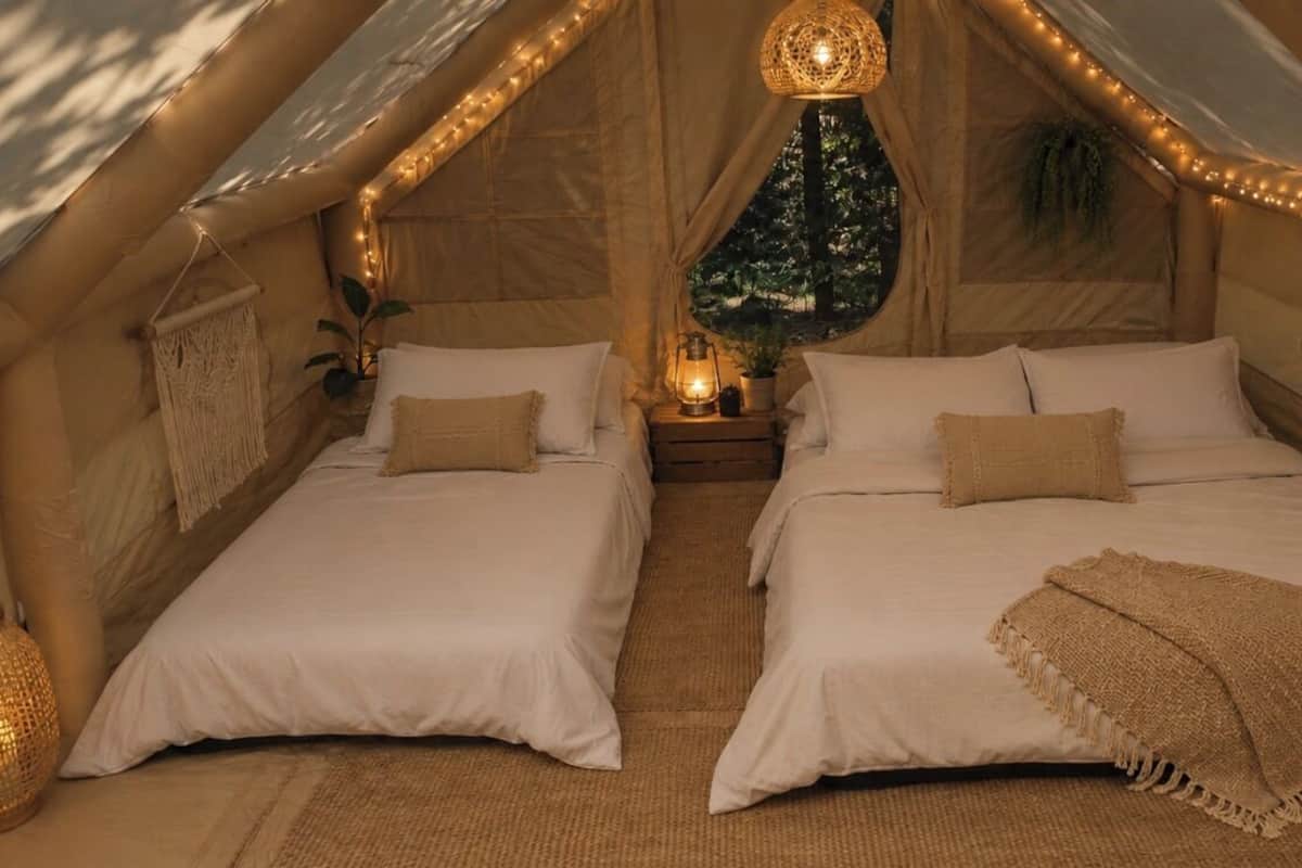 A cozy tent-style room with two beds, string lights, and a hanging lantern.