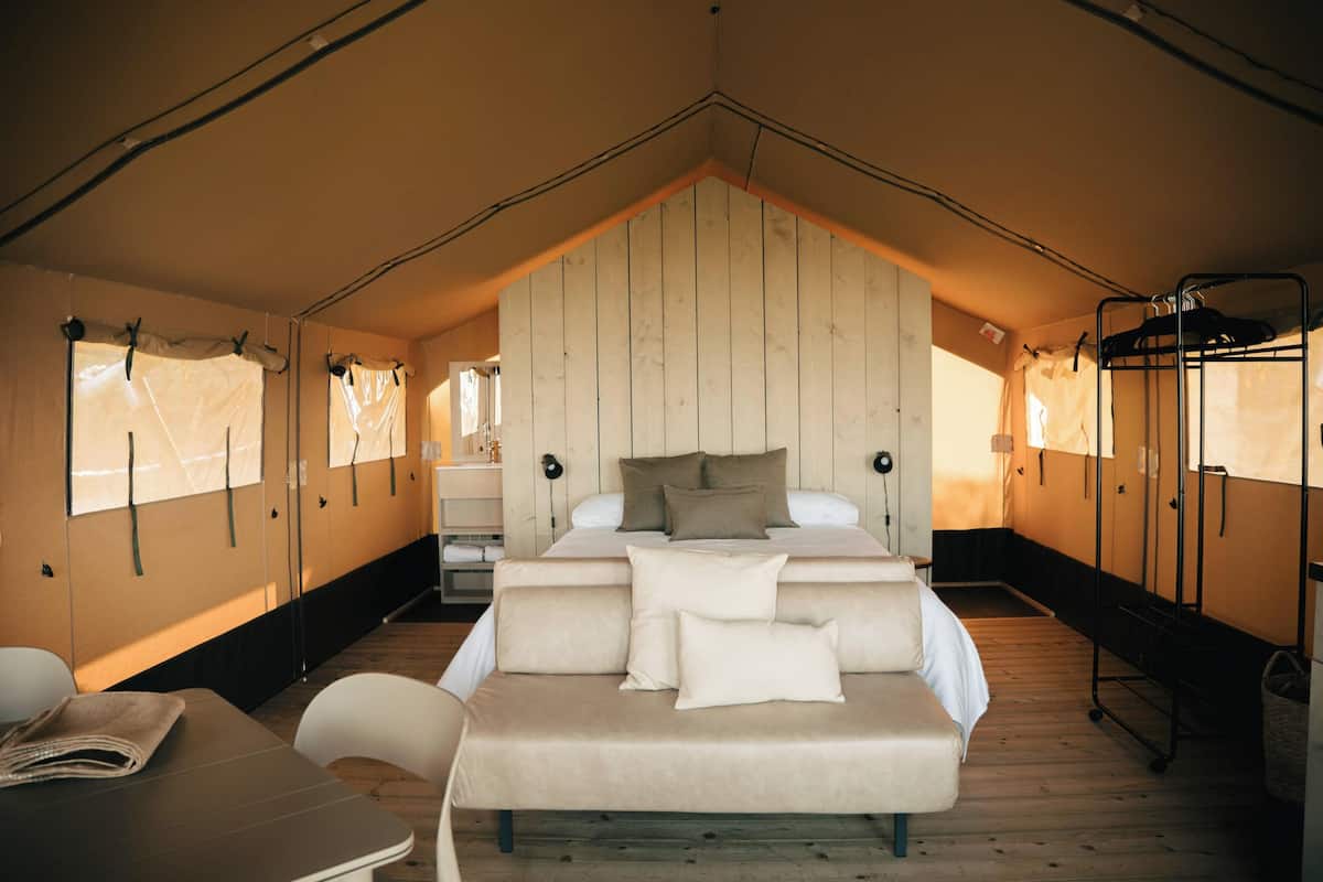 A tent-style room with a bed, a table, chairs, and a bunk bed.