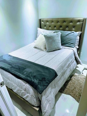A neatly made bed with a grey bedspread, a dark throw blanket, and two pillows. - Cozy basement apartment (Kitchener)