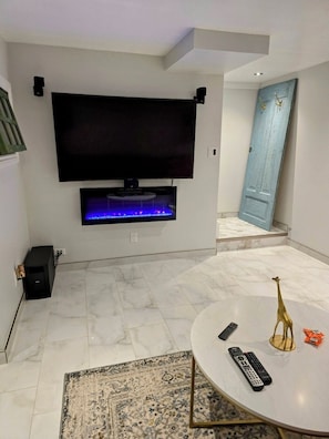 A modern living room with a flat-screen TV mounted on the wall, a marble floor, a round coffee table, and a small rug. - Cozy basement apartment (Kitchener)