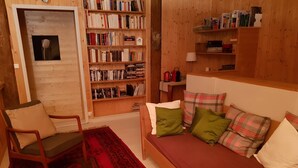 Et hyggeligt rum med en træbogreol, en rød sofa med mønstrede puder, en træstol og en rød, mønstret måtte.