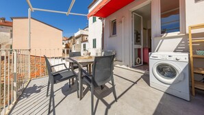 A balcony with a table and chairs, a washing machine, and a red awning. - Apartment 'Terraviva - La Terrazza Sul Nespolo' with Private Terrace, Wi-Fi and Air Conditioning (Cecina)