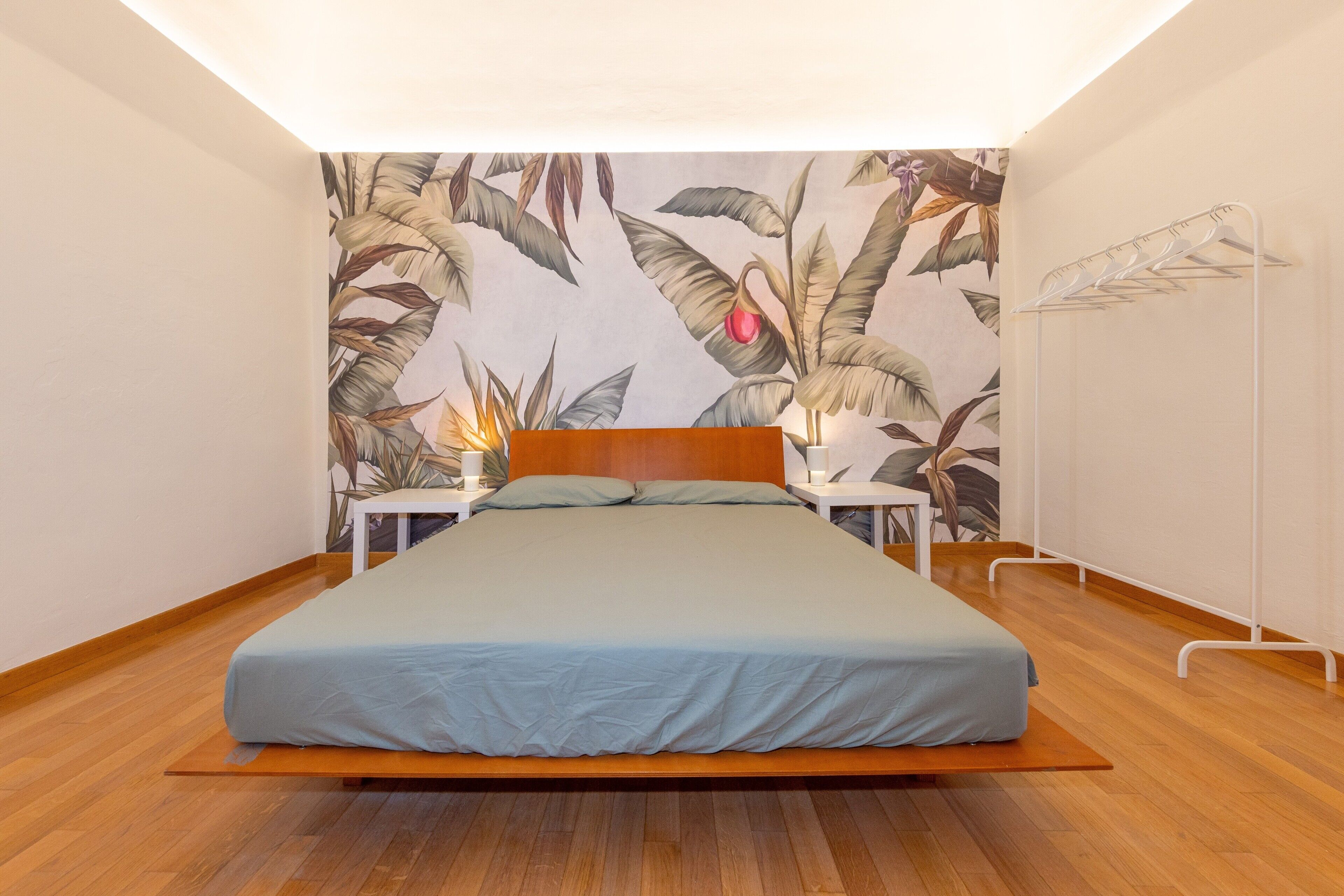 A bedroom with a bed, a nightstand, a lamp, and a wall-mounted drying rack.