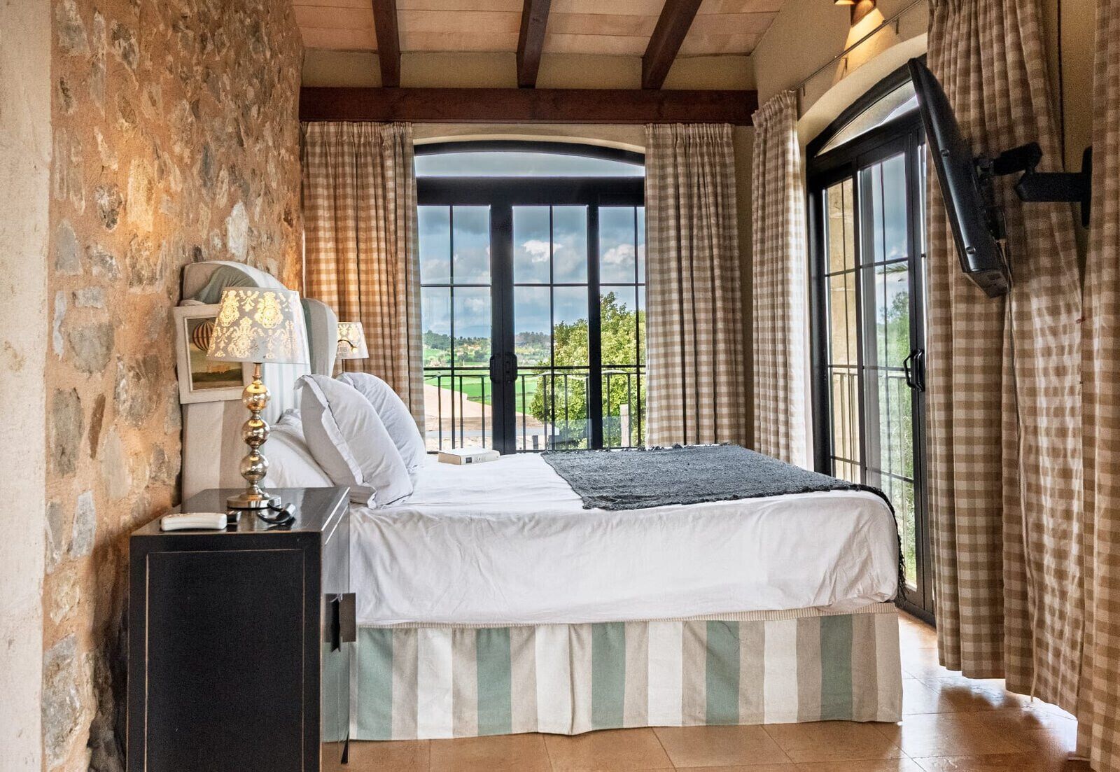Een slaapkamer met een groot raam, een bed met een gestreepte spreideken, een bedlampje en uitzicht op het landschap.