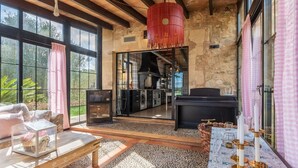 Amplia sala de estar con grandes ventanales, una chimenea y una cocina visible a través de una puerta abierta.