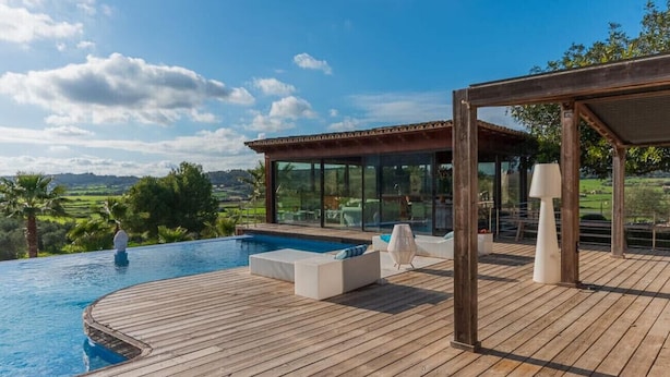 Una terraza de madera con piscina, mobiliario exterior y una estructura con paredes de vidrio.
