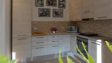 A modern kitchen with light wood cabinets, a microwave, and a stove. There are framed pictures on the wall and a small plant on the counter.