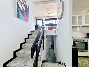 A staircase with black railings leading to a landing, a kitchen area with white cabinets, and a ceiling fan. - CASA BARBARA Roses / Roses - INTERimmo (Rosas / Roses)