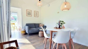 Een moderne woonkamer met een grijze bank, witte stoelen, een ronde tafel en twee hanglampen.