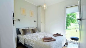 Een slaapkamer met een bed, een deur, een raam en uitzicht op de omgeving.