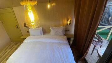 Habitación de hotel con cama, lámpara colgante, mesita de noche, lámpara de pared y vistas al exterior.