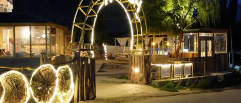 A nighttime entrance with a sign reading 'AYASH' and a glass structure with lights.