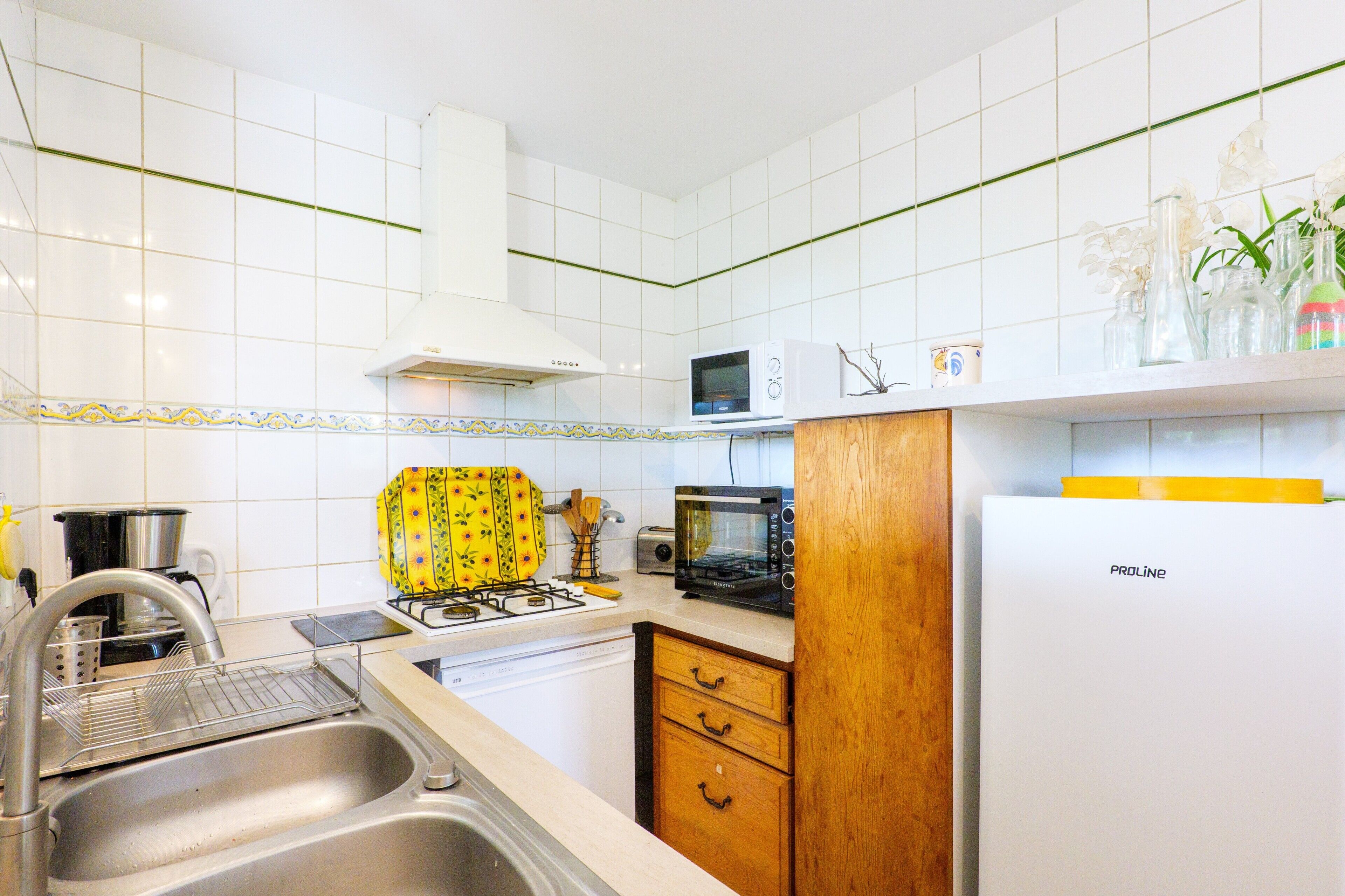 A kitchen with white tiles, a microwave, a toaster, a sink, and a refrigerator.