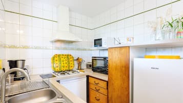 A kitchen with white tiles, a microwave, a toaster, a sink, and a refrigerator.