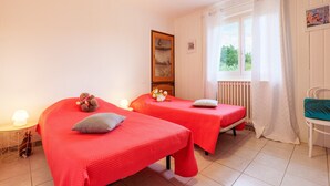 Ein Zimmer mit zwei Betten, einem Vorhangfenster, einem Heizkörper und einem Sessel.