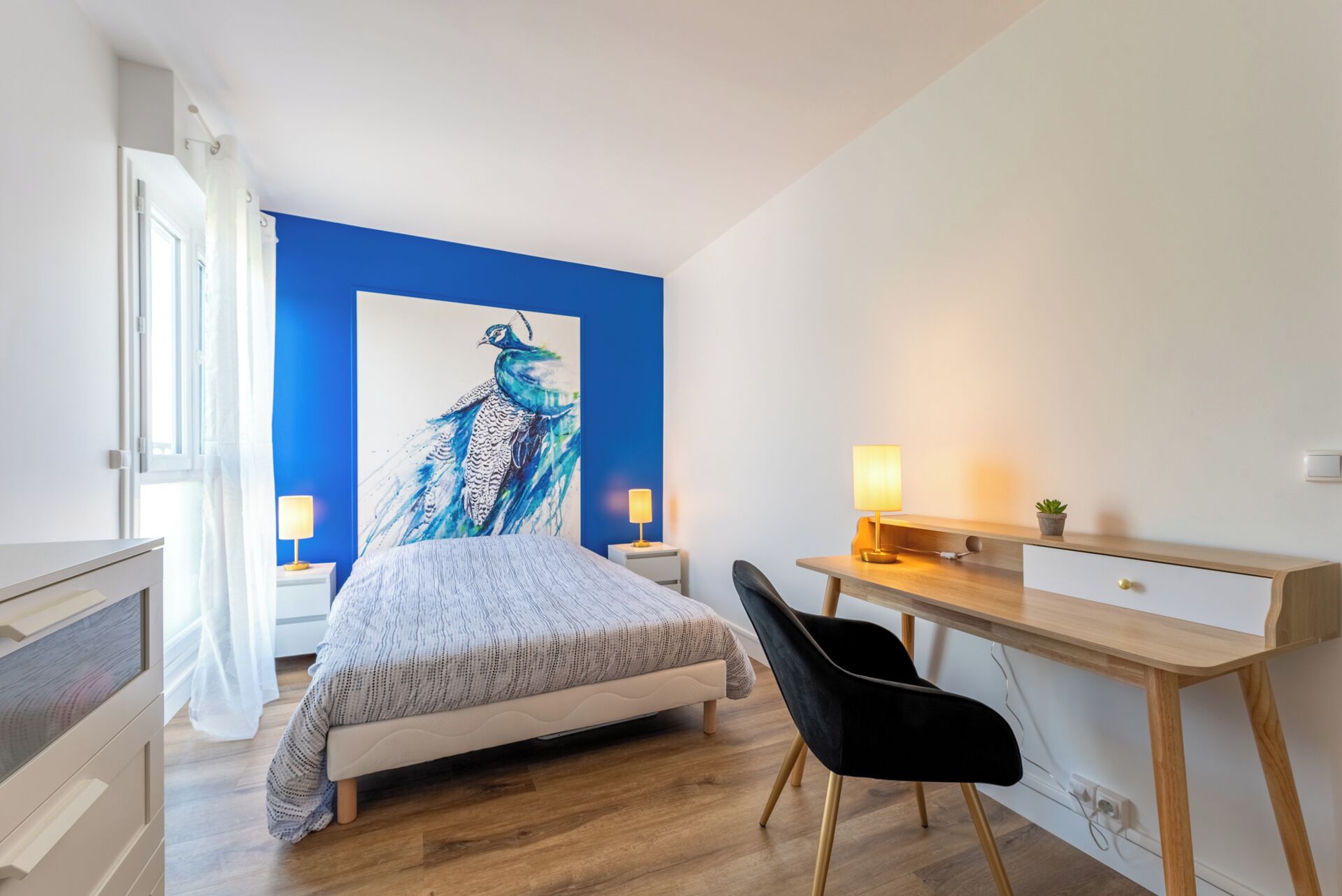 A bedroom with a bed, a desk, a chair, and a large painting on the wall.