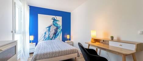 A bedroom with a bed, a desk, a chair, and a large painting on the wall.