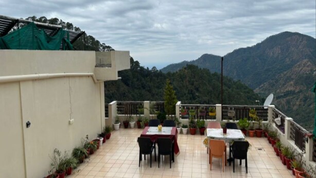 Une terrasse sur le toit, aménagée avec des tables et des chaises, des plantes en pot et offrant une vue sur les montagnes.