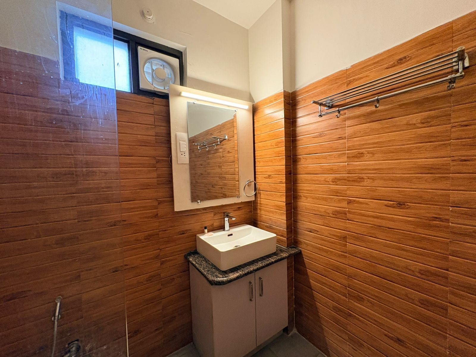 Un baño con paneles de madera, un lavamanos blanco, un espejo y un perchero para toallas.