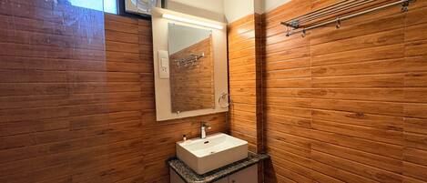 Un baño con paneles de madera, un lavamanos blanco, un espejo y un perchero para toallas.