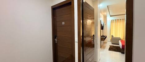Un pasillo con una puerta de madera marcada '314' que da a una habitación con una cama, un televisor y una ventana con cortinas.