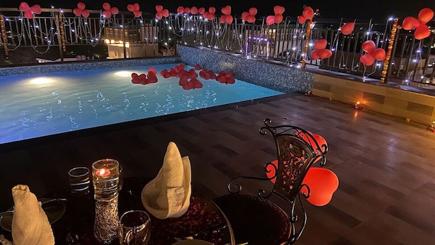 Un área de piscina al aire libre con zona de comedor, que incluye una mesa con velas y vasos, y una silla.