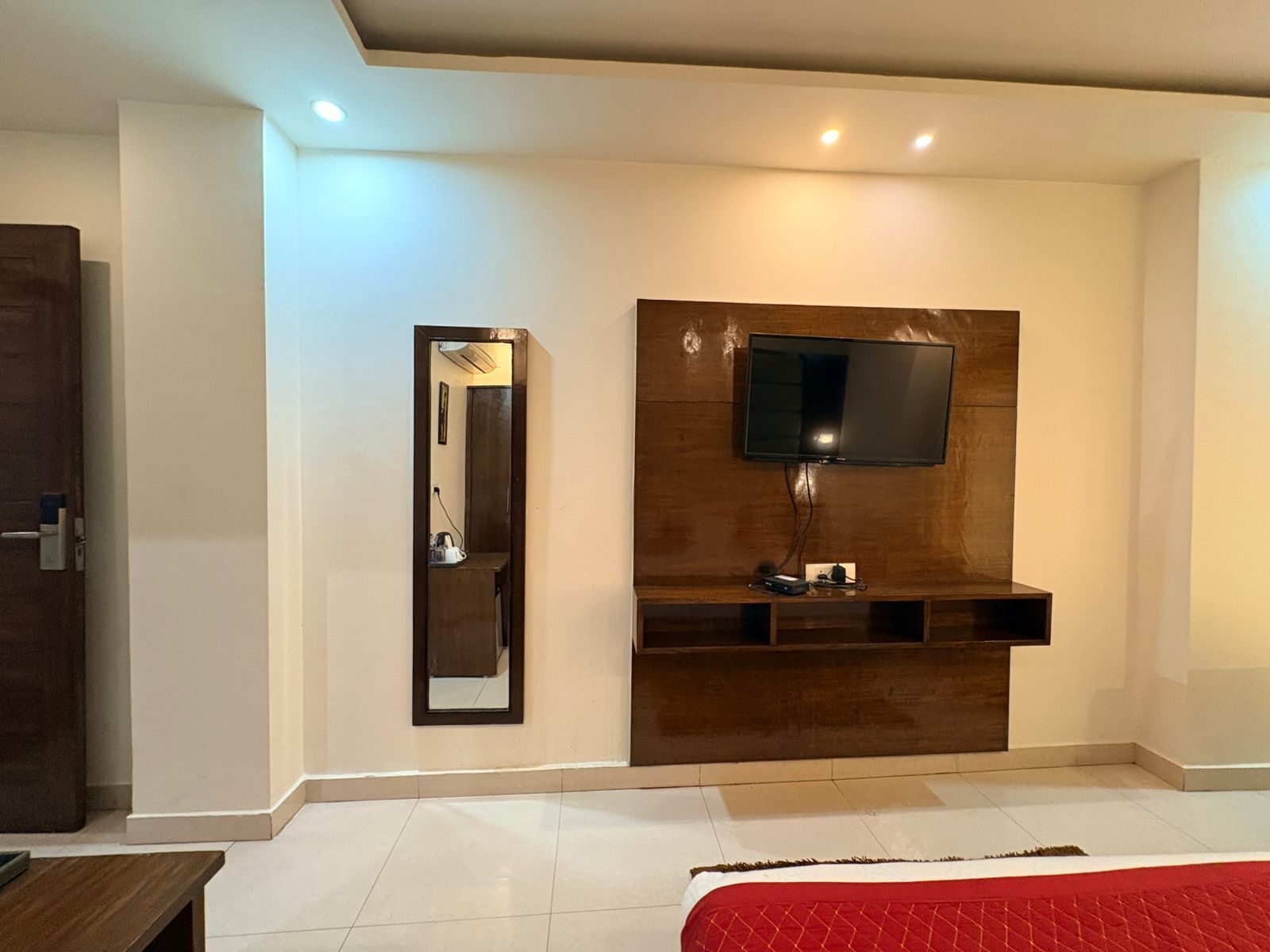 Une chambre à coucher moderne avec un mur d’accent en bois, un téléviseur fixé au mur, un miroir et une table de chevet.
